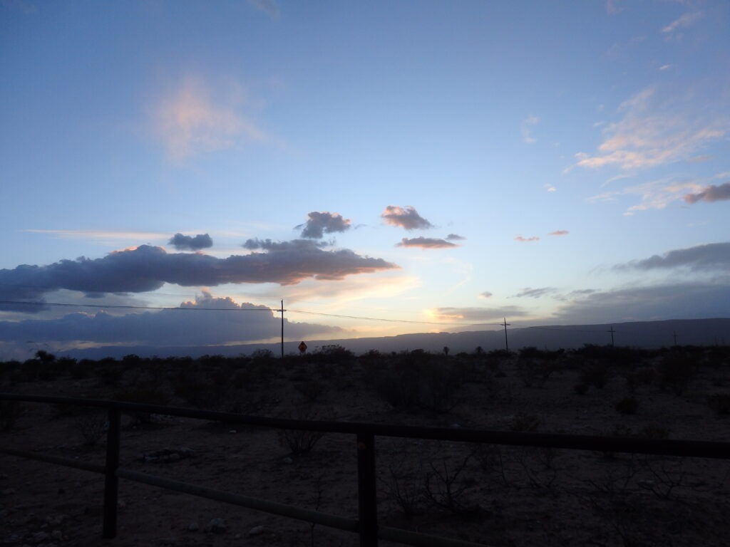 Colorful sunset sky with layered clouds over a desert landscape, featuring distant power lines and silhouetted shrubs. Ideal for nature and exploration content.