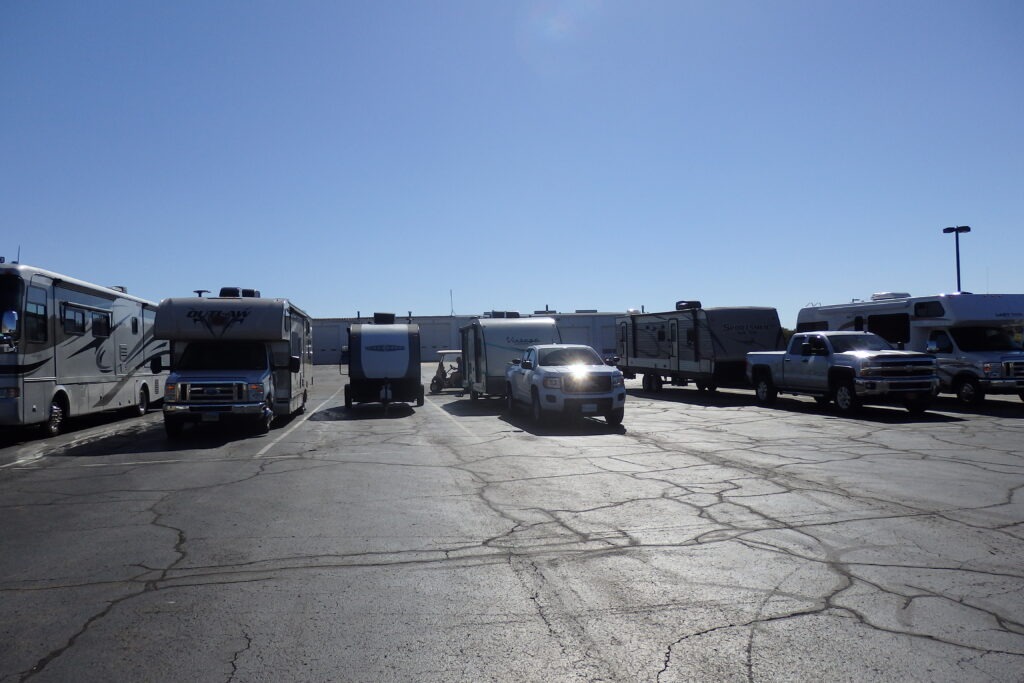 Several recreational vehicles and a pickup truck are parked in a large, sunny lot, showcasing options for outdoor travel or camping.